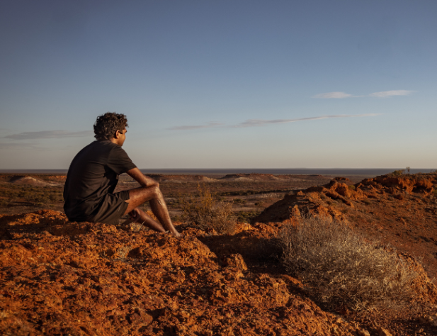 Aboriginal man sitting on rocky surface looking out at skyline